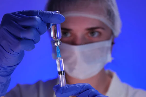 Mavi arka planda ilaç şişesi ve şırıngası olan üniformalı bir doktor.