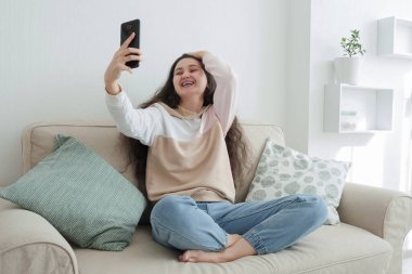 Genç bir kadın evinde, kanepede otururken arkadaşlarıyla video konuşarak eğleniyor. İnternette sohbet ediyoruz. Çevrimiçi yaşam