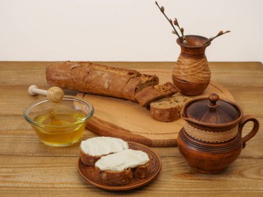 Ahşap bir masada toprak takımında kahvaltı. Kırsal doğal ürünler, baget, bal, el yapımı kil sürahide süt.