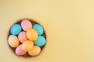Renkli Paskalya yumurtaları, sarı arka plandaki sepetin içinde pastel tonlarda. Boşluğu kopyala, üst görünüm, düz uzanma
