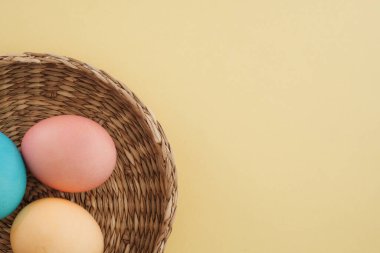 Fotokopi alanı, üst görünümü ve düz yatağı olan sarı trend arka planda hasır sepetteki Paskalya renkli yumurtalar