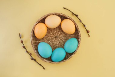 Basket with Easter eggs in pastel yellow and blue shades and pussy willow branches on a pale yellow background. Easter composition