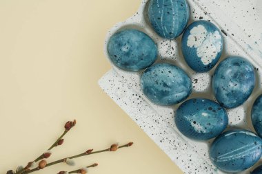 Stylish easter background with painted blue eggs and pussy willow branches on pastel yellow backdrop
