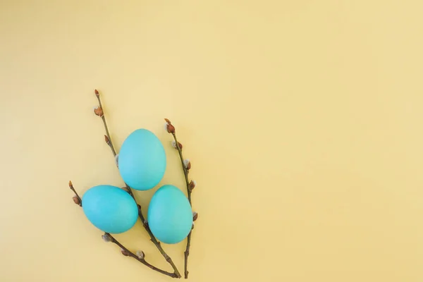 Blue easter eggs and pussy willow branches are laid out in the form of a bouquet on a gentle yellow background with a place for text, top view, flat lay