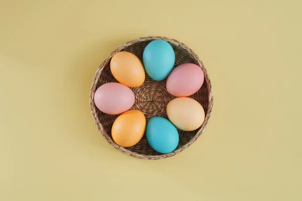 Renkli Paskalya yumurtaları pembe, sarı ve mavi tonlarda pastel sarı arka planda bir sepette. Üst manzara, düz uzanma