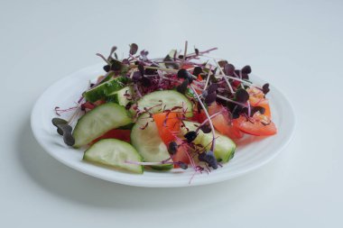 Beyaz bir masada beyaz bir tabakta taze salata, mikro yeşiller ve sebzeler.