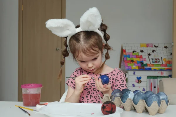 Tavşan kulaklı kız evde suluboya yumurta boyuyor.