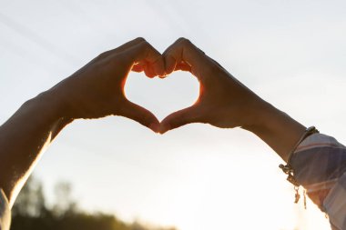 Yazın günbatımında aşk dolu bir kalbe benzeyen kadın elleri silueti.