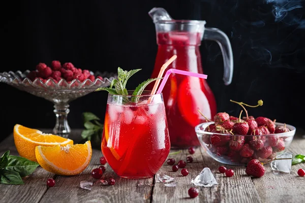 Cocktail of berry juice, orange and peppermint on a wooden background