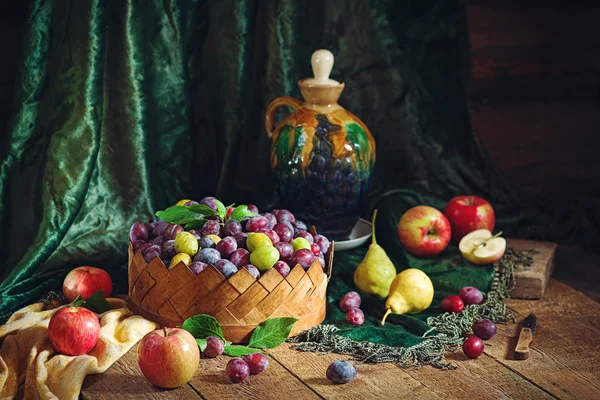 Nature morte avec prunes dans un panier et fruits dans un style rustique — Photo