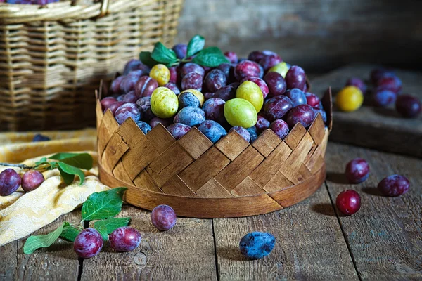 Prunes mûres dans un panier sur une surface en bois — Photo