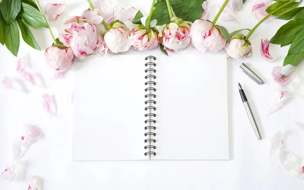 Flatlay office desk. Workplace with peonies, petals and block note. Open note book or diary and pen. Top view with copy space. Plan writing concept.