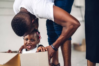 Mutlu aşk portresi Afro-Amerikan ailesi Afrikalı baba ve anne küçük Afrikalı kız gülümsüyor yeni evdeki karton kutuda oturuyorlar taşınırken bavullarını boşaltıyorlar ve eğleniyorlar.