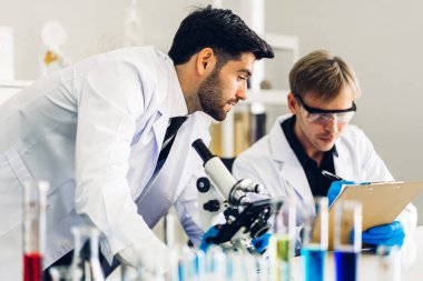 Profesyonel iki bilim adamı test tüpünde sıvı analiz ederken ve karıştırırken kimyasal bir deney yapıyor. Genç bilim adamı laboratuvarda cam üzerine kimyasal örnekler bırakıyor.