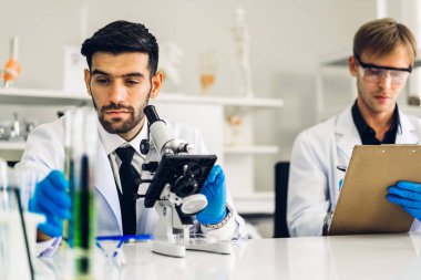 Profesyonel iki bilim adamı test tüpünde sıvı analiz ederken ve karıştırırken kimyasal bir deney yapıyor. Genç bilim adamı laboratuvarda cam üzerine kimyasal örnekler bırakıyor.