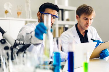 Profesyonel iki bilim adamı test tüpünde sıvı analiz ederken ve karıştırırken kimyasal bir deney yapıyor. Genç bilim adamı laboratuvarda cam üzerine kimyasal örnekler bırakıyor.