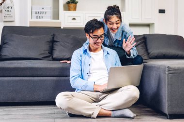 Genç Asyalı çift dizüstü bilgisayarlarını kullanarak rahatlıyor. İnternetteki video konferansında sohbet ediyorlar. Evde yaratıcı iş çifti planlama ve beyin fırtınası yapıyorlar.