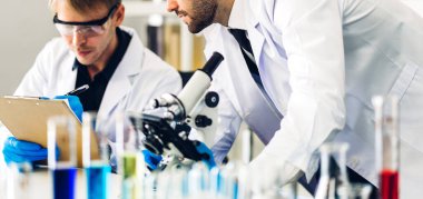 Profesyonel iki bilim adamı test tüpünde sıvı analiz ederken ve karıştırırken kimyasal bir deney yapıyor. Genç bilim adamı laboratuvarda cam üzerine kimyasal örnekler bırakıyor.