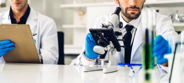 Profesyonel iki bilim adamı test tüpünde sıvı analiz ederken ve karıştırırken kimyasal bir deney yapıyor. Genç bilim adamı laboratuvarda cam üzerine kimyasal örnekler bırakıyor.