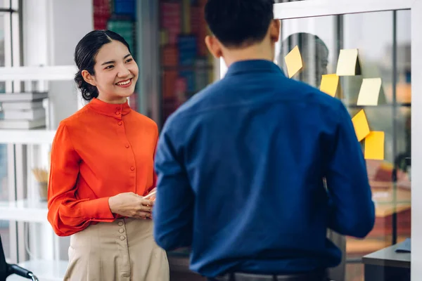 カジュアルな創造的な幸せな2つの笑顔アジアのビジネスの人々戦略分析とブレインストーミングを計画する人々は 現代のオフィスでガラス基板上のスタートアッププロジェクトのアイデアを共有するためにそれステッカーノートを置く — ストック写真