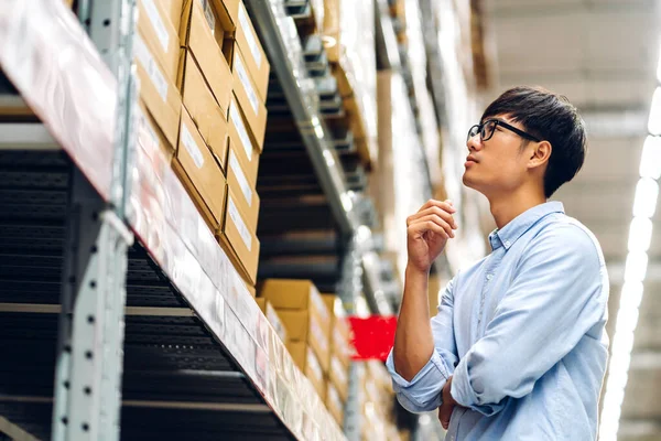 Portrait of smiling asian manager worker man standing and order details checking goods and supplies on shelves with goods background in warehouse.logistic and business export