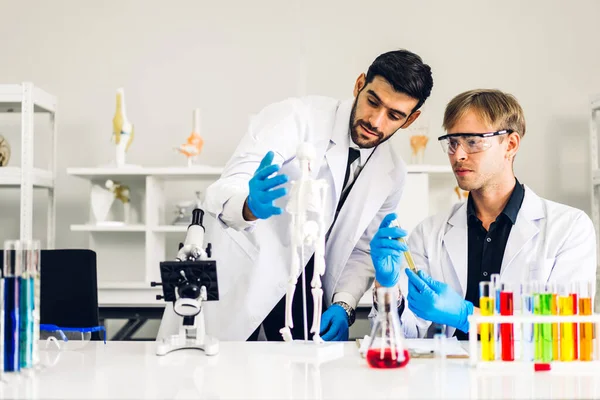 Professional two scientist man research and working doing a chemical experiment while making analyzing and mixing  liquid in test tube.Young science man dropping sample chemical on glass at laboratory