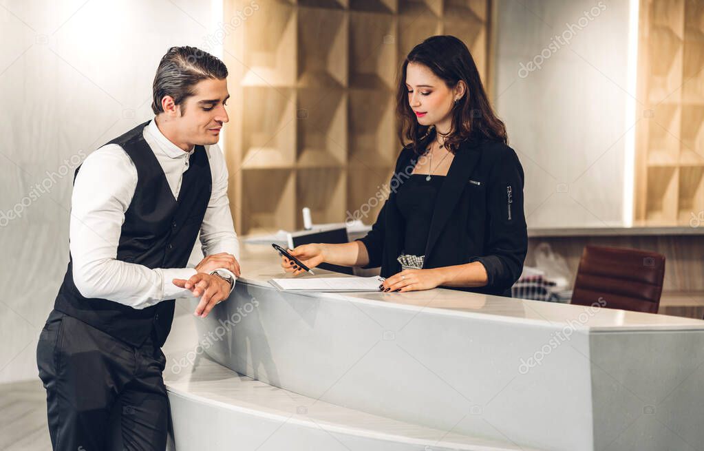 Young handsome businessman talking and check in Register information with woman receptionist worker standing in counter hotel reception counter desk at lobby modern hotel