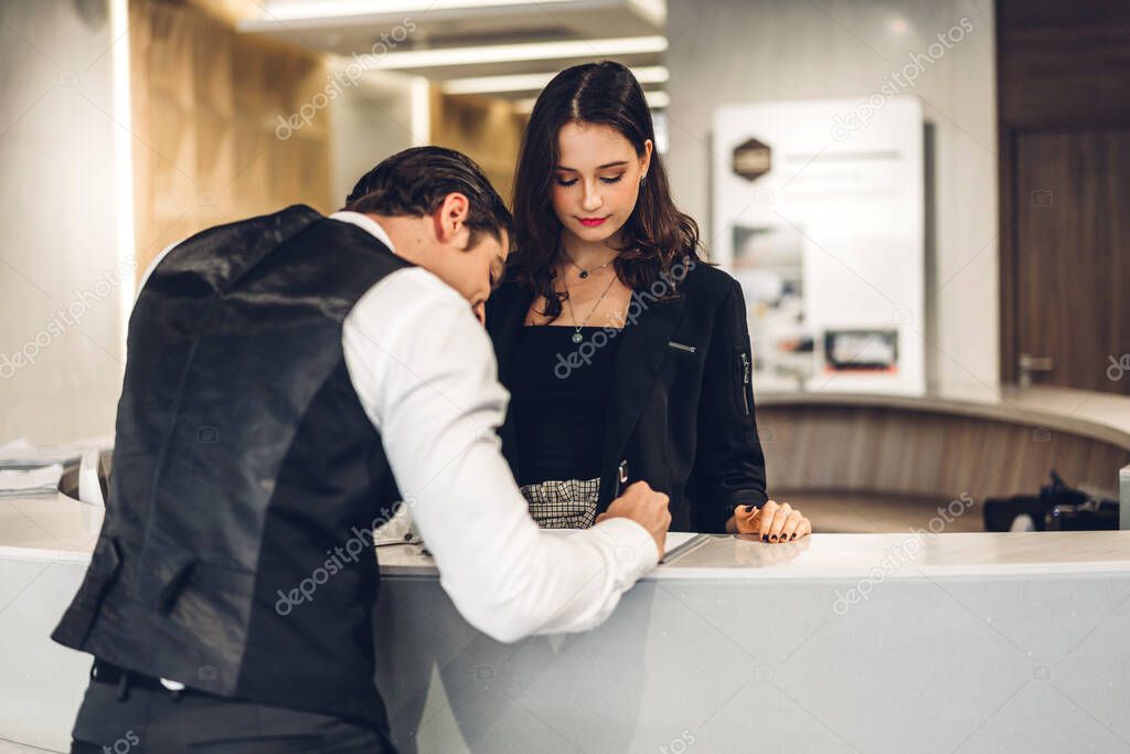 Young handsome businessman talking and check in Register information with woman receptionist worker standing in counter hotel reception counter desk at lobby modern hotel