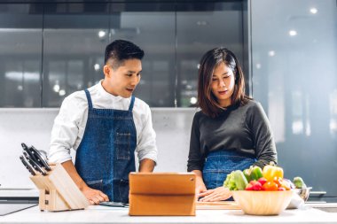 Genç Asyalı çift masada taze sebze salatasıyla birlikte yemek pişiriyor. Mutlu çift mutfakta lezzetli bir yemek hazırlıyor.