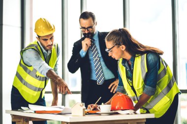 İnşaat alanındaki masanın üzerinde tasarım ve inşaat araçlarıyla çalışan miğferli kargo ustabaşıları.