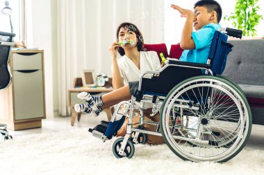 Mutlu aşk portresi. Asyalı anne oynuyor ve bakıcı tekerlekli sandalyede oturan engelli çocuğa bakıyor. Evde engelli bakımı konseptinde iyi vakit geçiriyor.