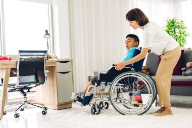 Asyalı fizyoterapistin portresi engelli çocuk sağlığı sorununa rehabilitasyon kliniğinde tekerlekli sandalyede oturarak yardım ve oyun oynayarak yardımcı oluyor.