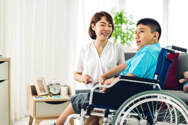 Asyalı fizyoterapistin portresi engelli çocuk sağlığı sorununa rehabilitasyon kliniğinde tekerlekli sandalyede oturarak yardım ve oyun oynayarak yardımcı oluyor.