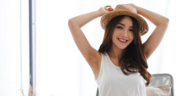 Gülümseyen güzel, güzel Asyalı kadın temiz, sağlıklı, beyaz tenli, beyaz elbiseli. Kız evde dinleniyor ve yatakta eğleniyor. Asya güzeli.