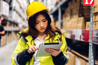 Gülümseyen Asyalı miğfer mühendisinin portresi, malzeme ve gereçlerin depo geçmişine sahip raflarda kontrol edilmesi için tablet bilgisayarından ayrıntılı talimat vermektedir. Lojistik ve ticari ihracat