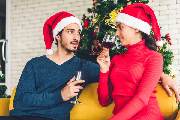 サンタの帽子のロマンチックな甘いカップルは 楽しいとワイングラスを飲みながら新年の前夜を祝い 自宅でクリスマスの時間に一緒に過ごすことを楽しんでいます — ストック写真