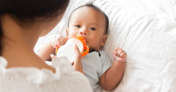 白い寝室でかわいい息子にミルクの母供給ボトル 家族の概念の愛 — ストック写真