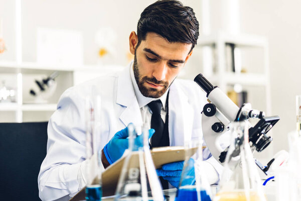 Professional scientist man research and working doing a chemical experiment while making analyzing and mixing  liquid in test tube.Young science man looking sample chemical on glass at laboratory