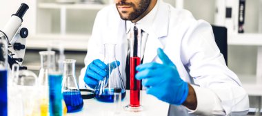 Profesyonel bilim adamı test tüpünde sıvı analiz ederken ve karıştırırken bir kimyasal deney yapıyor. Genç bilim adamı laboratuvarda cam üzerinde kimyasal örnekler arıyor.