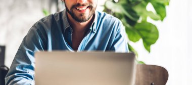 Yakışıklı sakallı hippi, kafeteryasında kahve olan dizüstü bilgisayarı kullanır ve ona bakar. İletişim ve teknoloji kavramı.