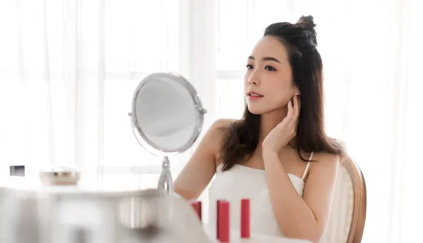 年轻美丽的亚洲女人微笑 洁白健康的肌肤 看着镜子 女孩用手触摸着脸 在家里涂上乳霜 — 图库照片