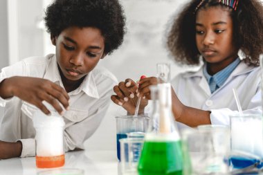 İki Afro-Amerikan tatlı erkek ve kız öğrenci araştırma yapmayı ve kimyasal deney yapmayı öğrenirken aynı zamanda fen bilimleri dersinde sıvıyı analiz edip karıştırıyorlar. Eğitim ve bilim konsepti.