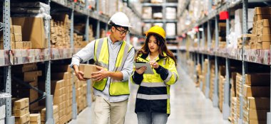 Miğfer mühendisi Asyalı iki mühendis, malzeme ve malzemelerin depo geçmişine sahip raflarda kontrol edilmesi için tablet bilgisayardan talimat verdi. Lojistik ve ticari ihracat