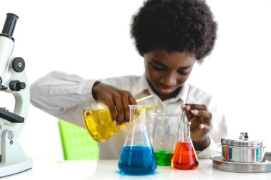 Afrika kökenli, sevimli, küçük bir çocuk. Araştırma yapmayı öğreniyor ve kimyasal bir deney yapıyor. Fen bilimleri sınıfında sıvıyı analiz edip karıştırıyor.