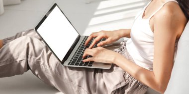 Asyalı kadın evinde dizüstü bilgisayar kullanarak rahatlıyor. Beyaz model boş ekranlarla çalışıyor. Teknoloji ve iletişim kavramı.