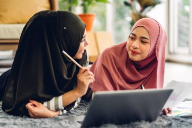 Genç, gülümseyen mutlu Asyalı Müslüman kadın evde dizüstü bilgisayar, tablet çalışma ve video konferans kullanarak rahatlıyor. Ev konseptinden iş.