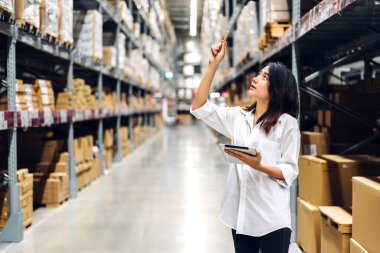 Gülümseyen Asyalı yönetici kadın portresi ayakta duruyor ve malzeme ve gereçleri depoda kontrol etmek için tablet bilgisayardan ayrıntılı talimat veriyor. Lojistik ve iş ihracatı