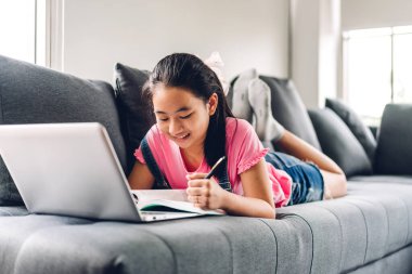 Okul çocuğu küçük kız öğreniyor ve dizüstü bilgisayara bakıyor ev ödevi yapıyor çevrimiçi eğitim sistemi ile bilgi öğreniyor. Evde öğretmenle çocuk video konferansı