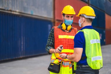 Koronavirüs için karantinada koruma maskesi takıp çalışmadan önce personel için alkol jeliyle ellerini yıkayan kasklı iki kargo ustabaşının profesyoneli.