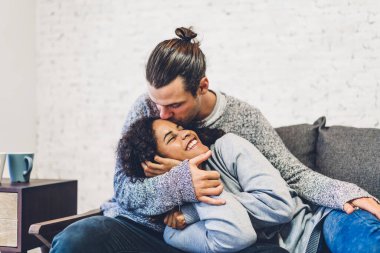 Romantik, genç, mutlu aşk çifti Kafkasyalı erkek ve Afrikalı Amerikalı kadın gülümseyip sevgililer gününde evde yatakta kucaklaşırken eğleniyorlar.